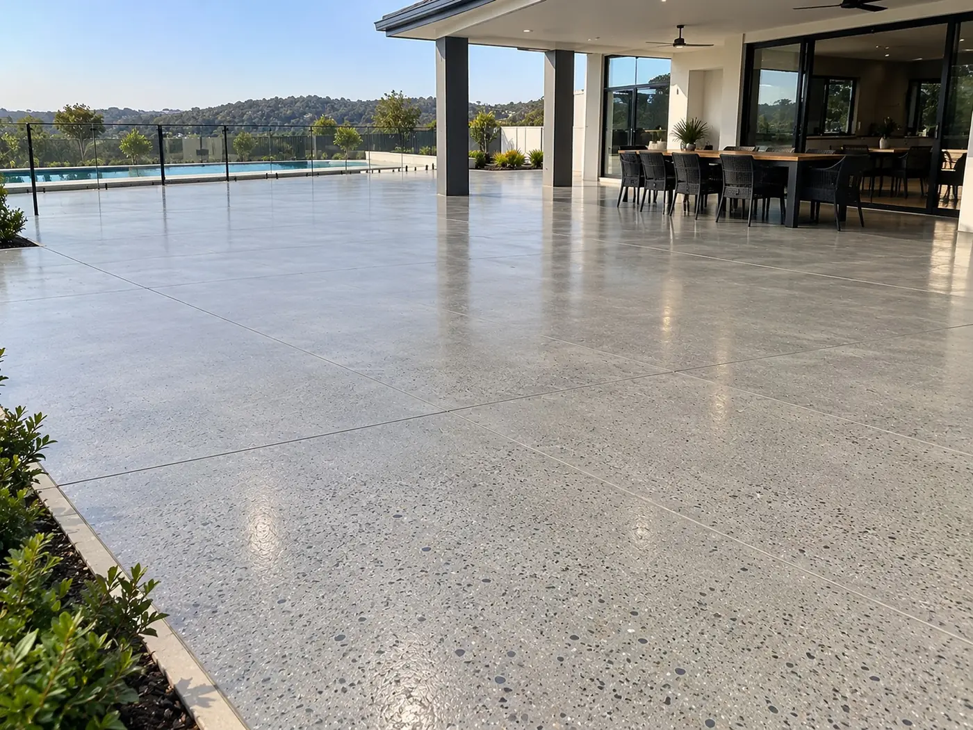Honed concrete patio beside an outdoor dining area and pool fence